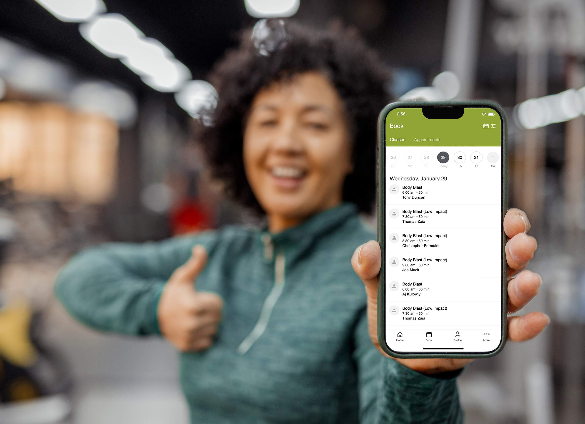 Lady holding a thumbs app showing an Iphone screen of the BodyScience app class schedule